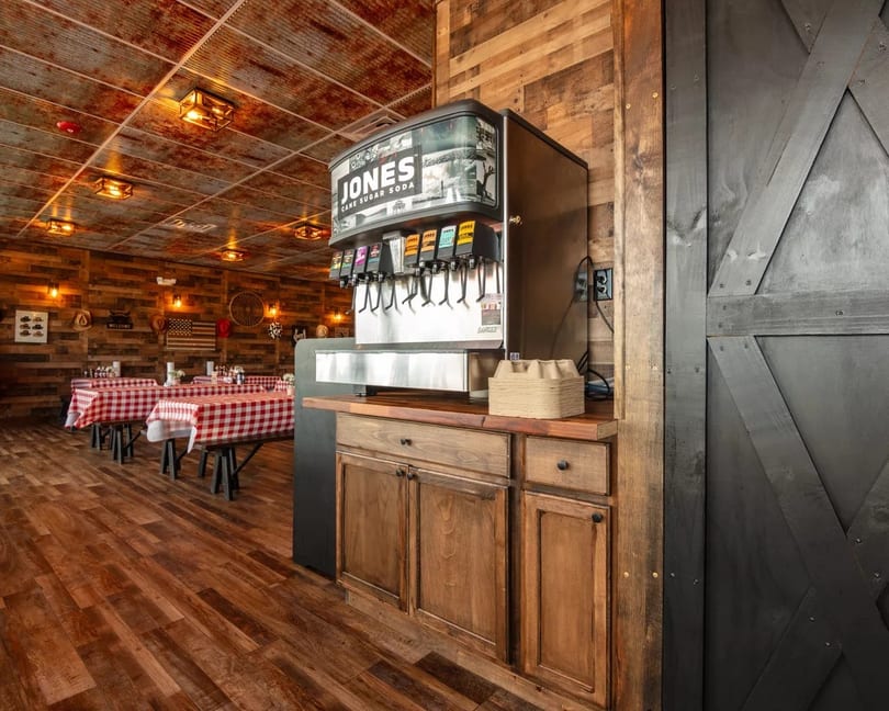 Rustic restaurant interior with a Jones Cane Sugar Soda machine, wooden walls, and red checkered tablecloths.