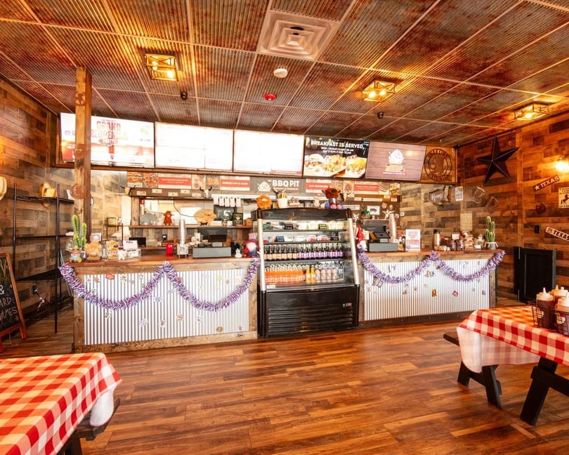 Rustic BBQ restaurant interior with corrugated metal and wood walls, decorated counter, and picnic tables.